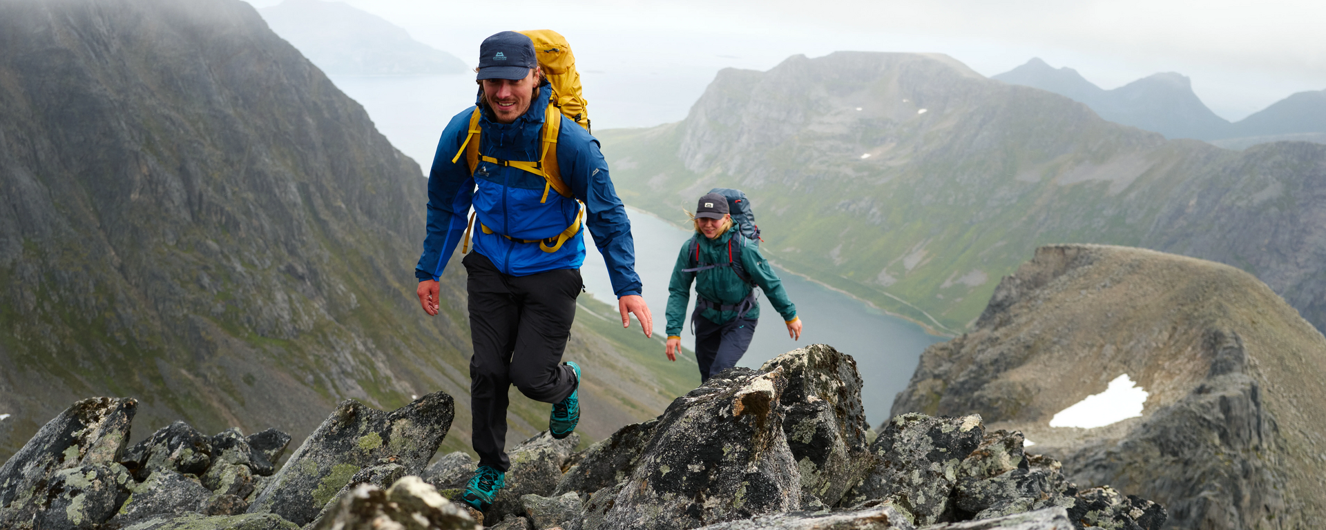 Zwei Bergsteiger, die in Norwegen einen schroffen Berg hochwandern und dabei die Raintower Jacket von Mountain Equipment in den Farben blau und grün tragen.