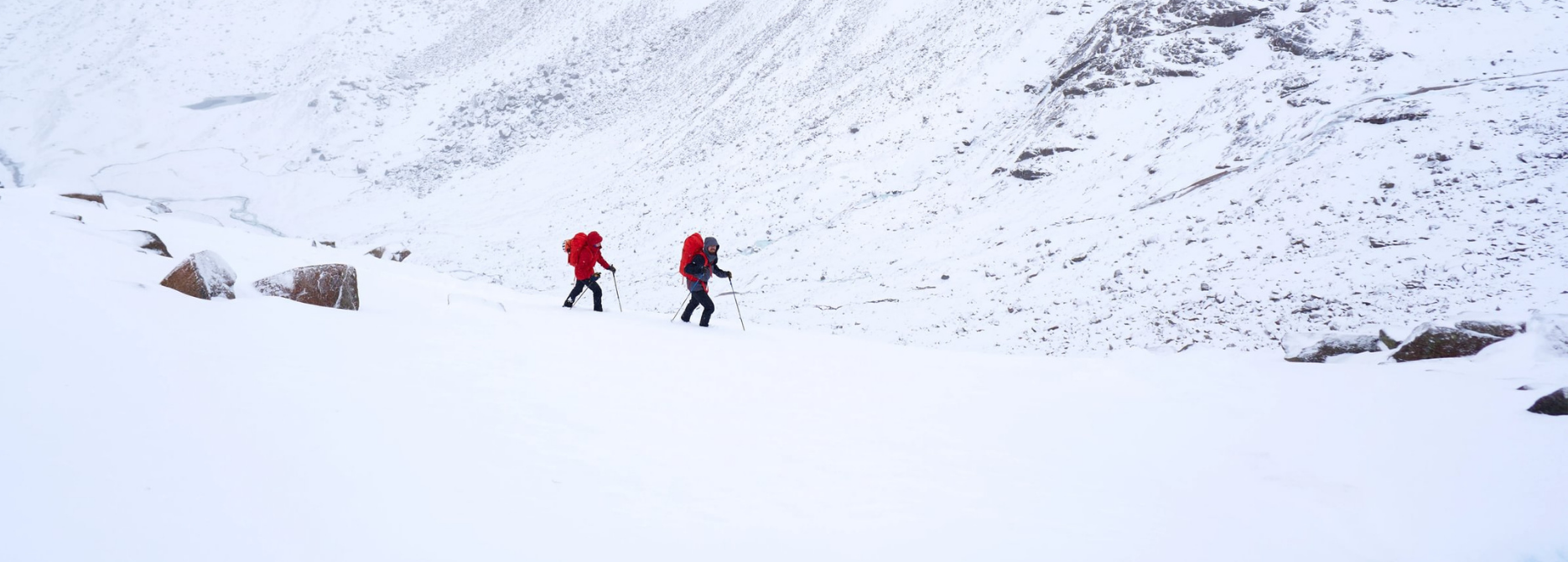 Zwei Bergsteiger in verschneiten Bergen, die in Richtung Gipfel steigen.