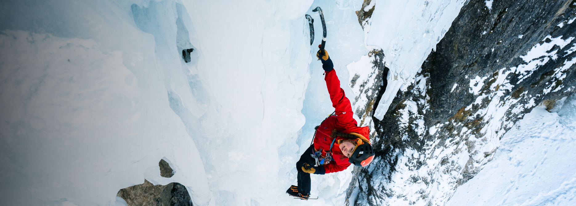 Eine Kletterin in einer roten Hardshelljacke Orion von Mountain Equipment. 