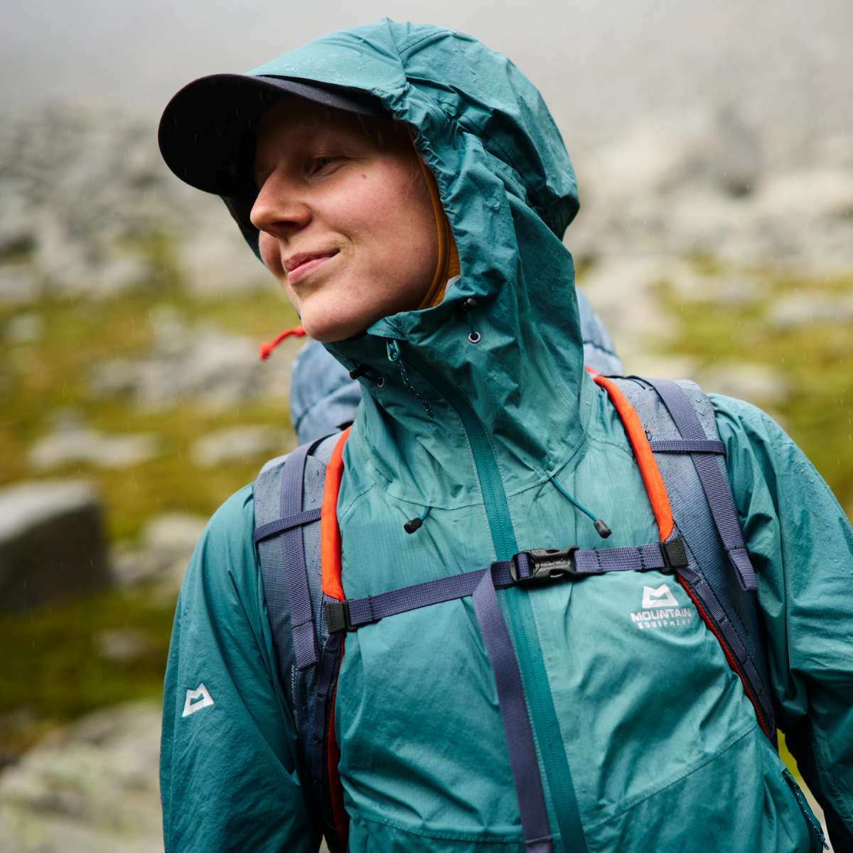 Eine junge Frau mit der Regenjacke Raintower in dunkelgrün von Mountain Equipment.